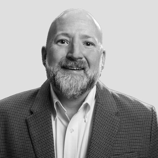 Smiling bald man with a beard in a checked blazer and white shirt, facing the camera.